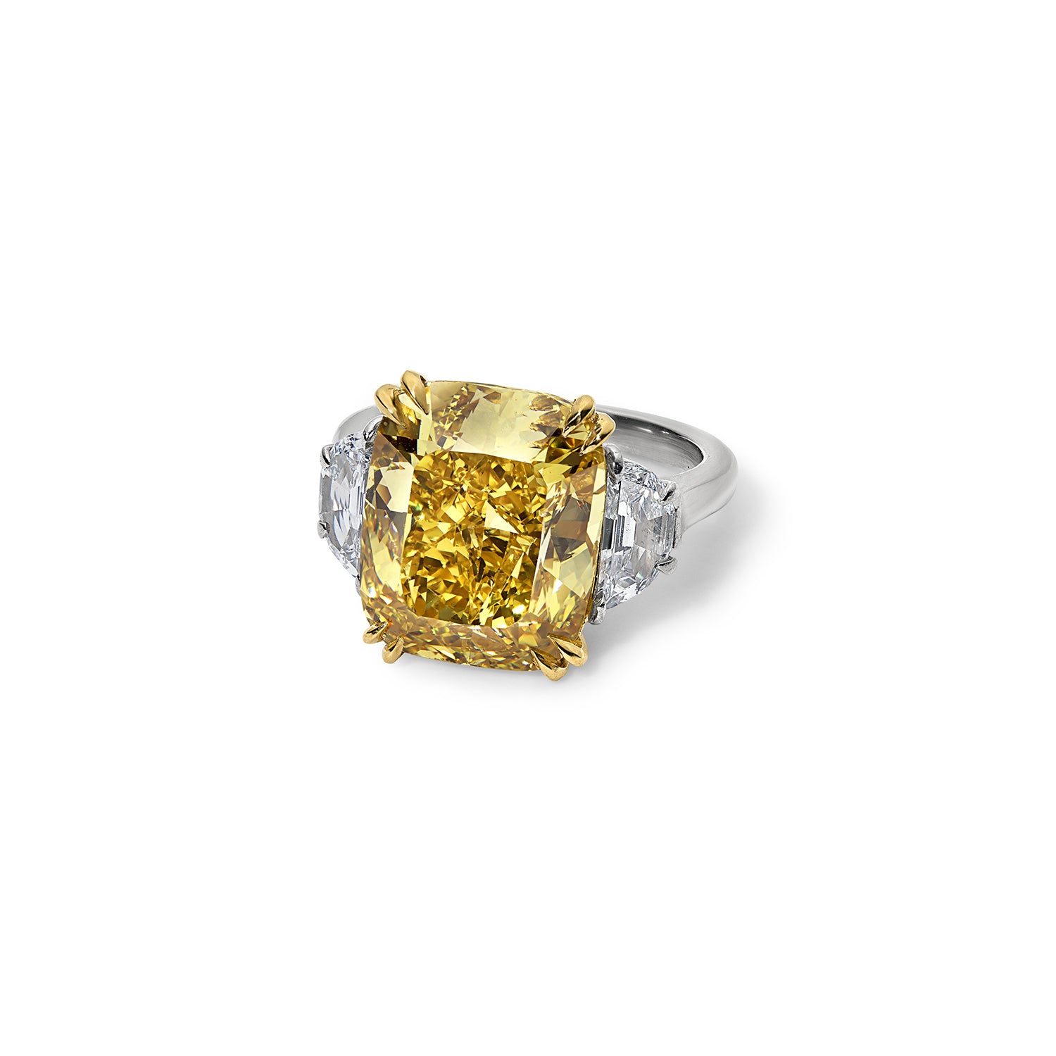 Front three-quarter view of a superb 6.80 carat vivid yellow diamond three stone ring, featuring colorless trapezoid cut diamonds in a handmade platinum and yellow gold setting.