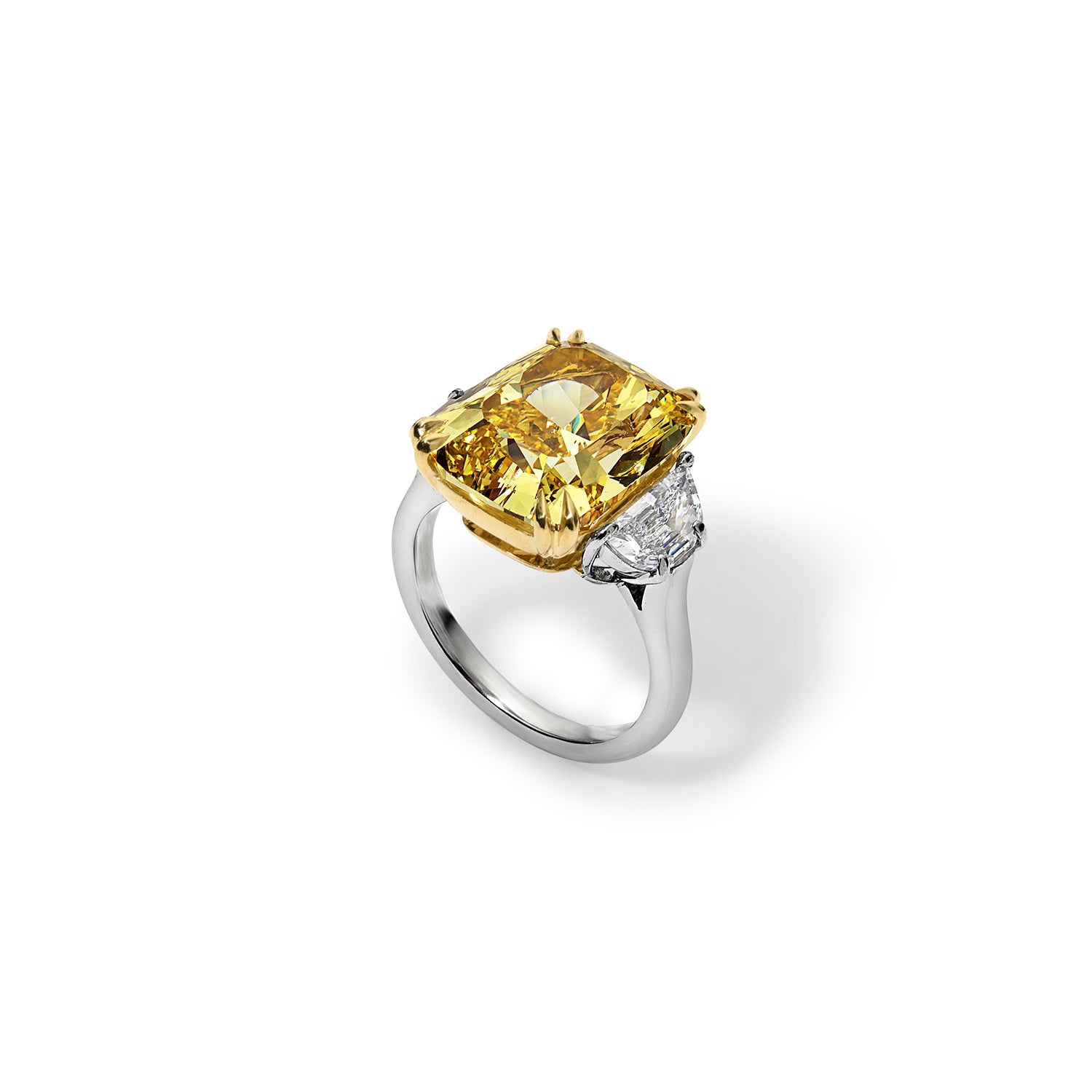 Top view of a 6.80 carat vivid yellow diamond three stone ring, adorned with colorless trapezoid cut diamonds and set in handmade platinum and yellow gold.